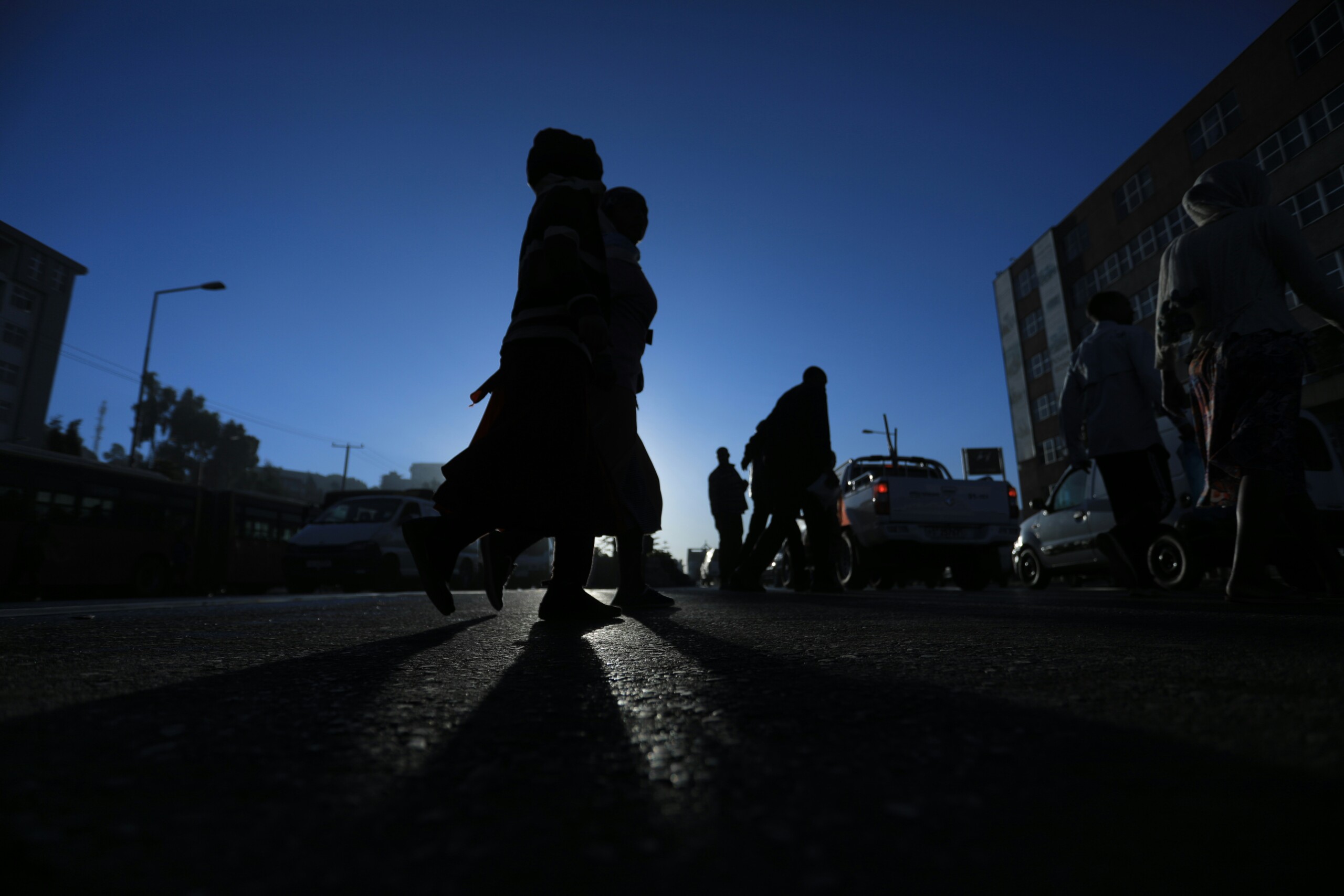 Silhouetter of people walking in a street under a blue sky