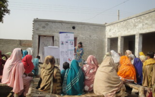 Community mobilization in the Family Advancement for Life and Health FALAH project – Population Council A group of women outside listening to a presentation.