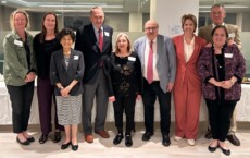 Group of ten professionals in business attire posing together in a bright office setting for a group photo at a reception event.
