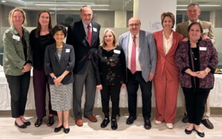 Group of ten professionals in business attire posing together in a bright office setting for a group photo at a reception event.