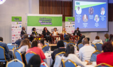 Panelists talking on the stage in the background with groups of attendees in the foreground.